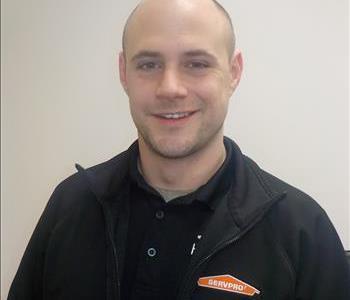 Headshot of smiling man in black Servpro polo in front of white wall